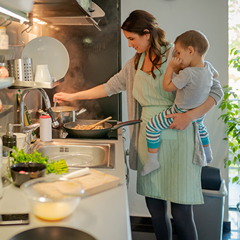 Mother holding child while cooking in kitchen